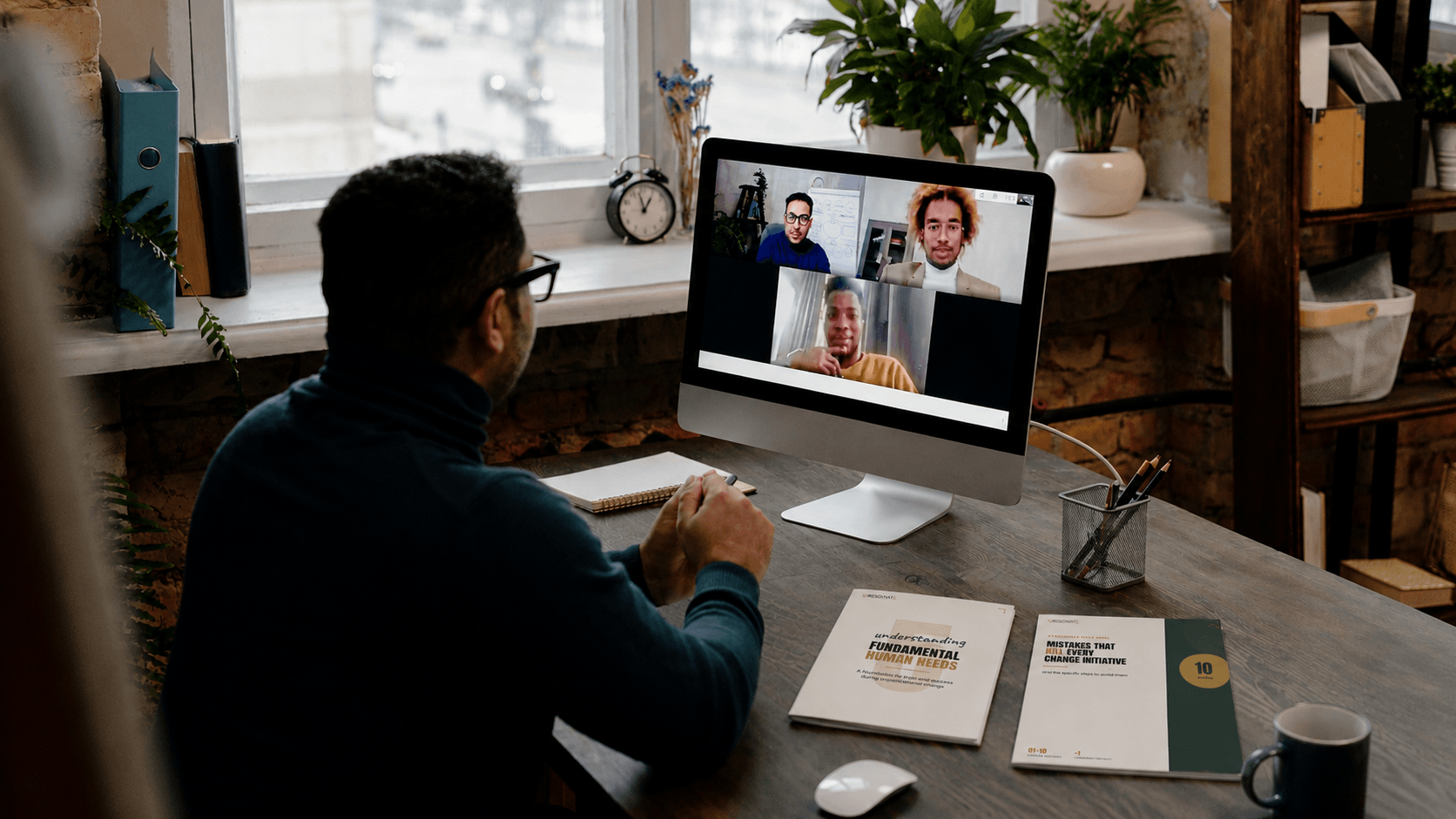 A leader on a video call with printed Wresonate guides — Understanding Fundamental Human Needs and 10 Mistakes That Kill Every Change Initiative — open on the desk beside him